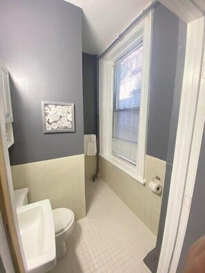 A bathroom with a toilet, a sink, a window with blinds, and a towel rack. - Perfect For Solo Travelers Or Friends! (Boston)