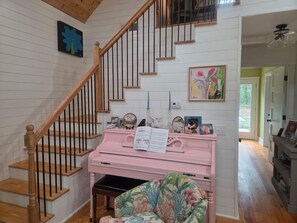 Una escalera con barandas de madera, un piano rosa y una silla con un estampado colorido.