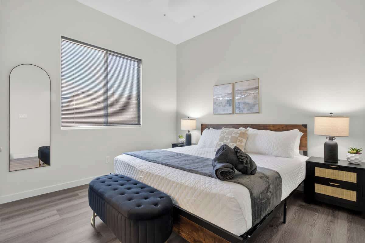A bedroom with a bed, a bench, a nightstand, a lamp, and a mirror.