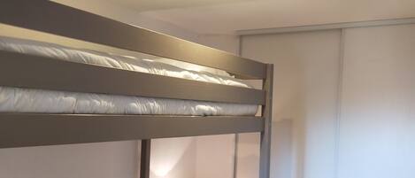 Een slaapkamer met een stapelbed, een nachtkastje met een lamp en een schuifdeur.