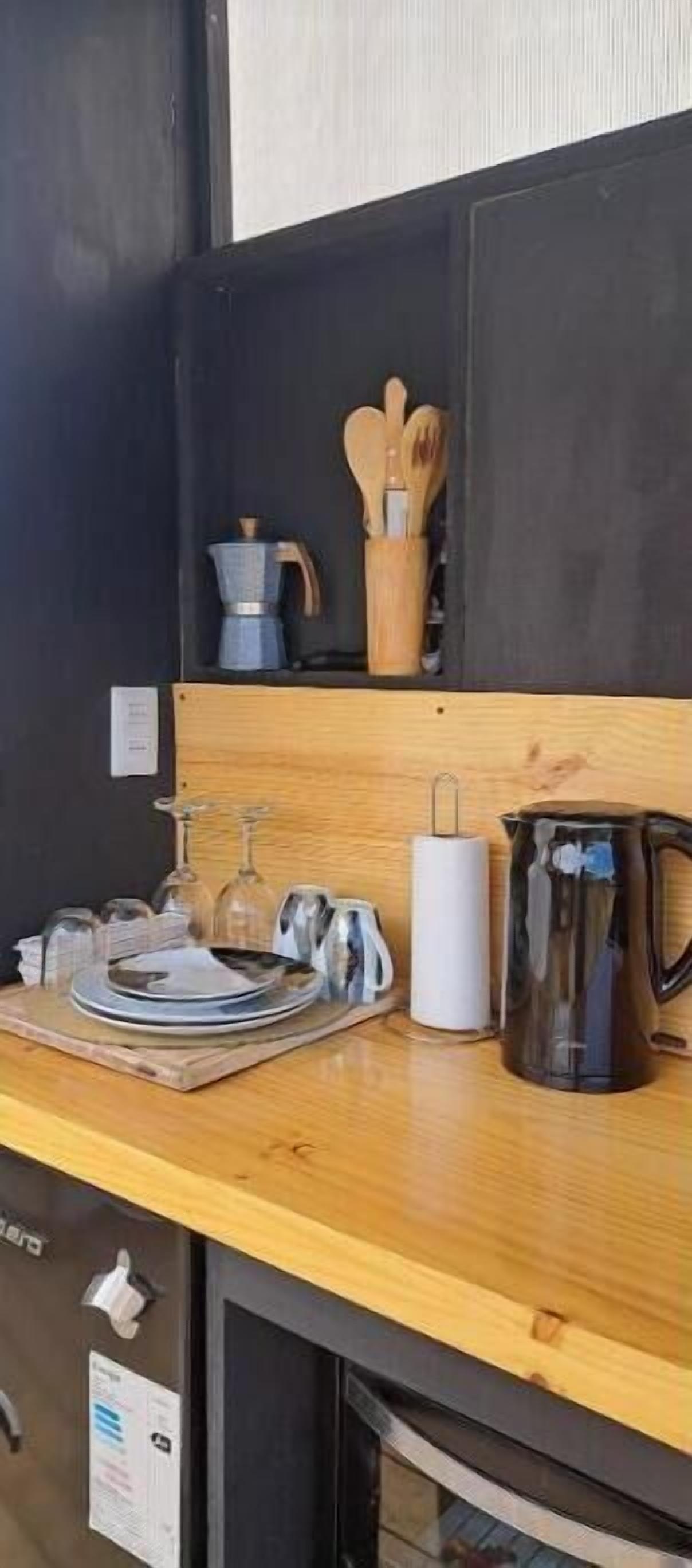 Una cocina con encimera de madera, una cafetera, un hervidor, un juego de utensilios y un frasco de vidrio.