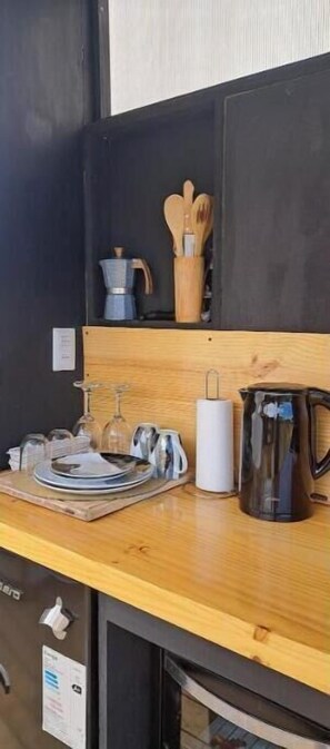A kitchen with a wooden countertop, a coffee pot, a kettle, a set of utensils, and a glass jar.