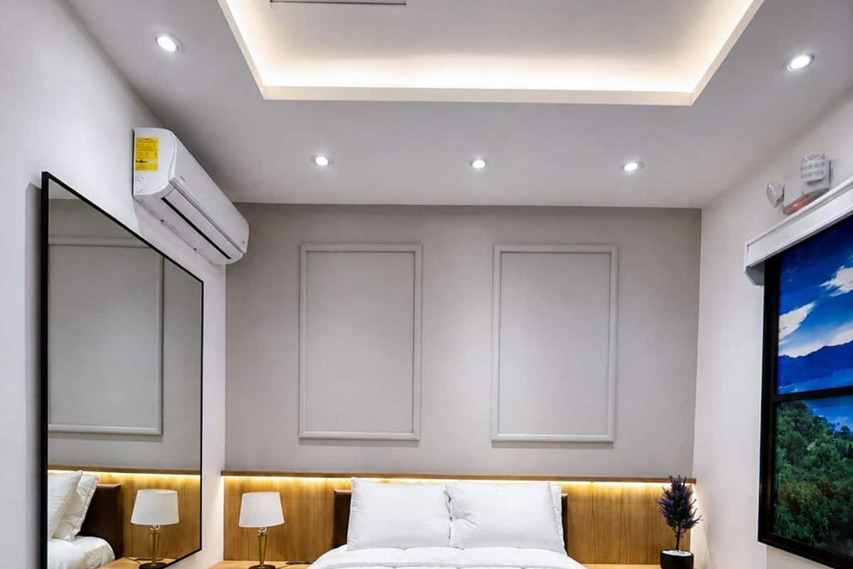 Un dormitorio moderno con una cama central, mesitas de noche, un espejo grande, un equipo de aire acondicionado y una lámpara en el techo.