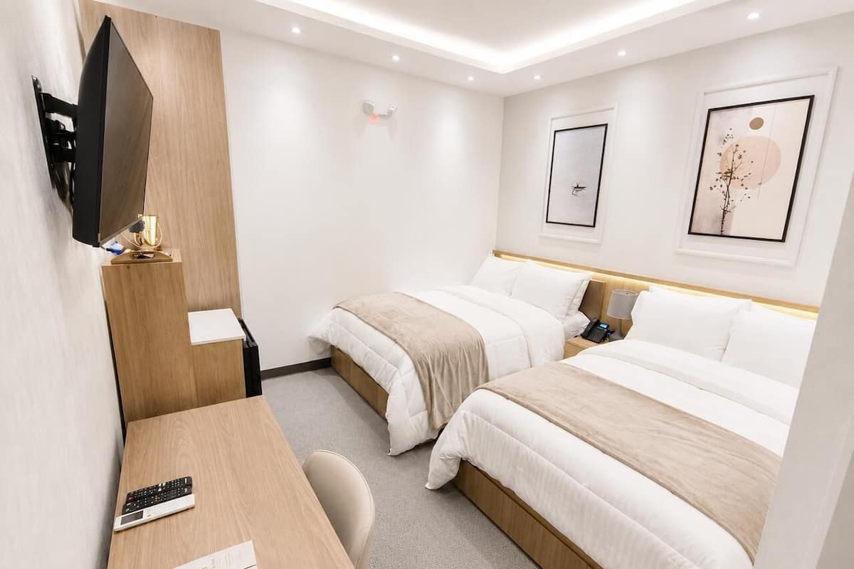 A hotel room with two beds, a desk with a keyboard, a TV mounted on the wall, and framed artwork on the walls.