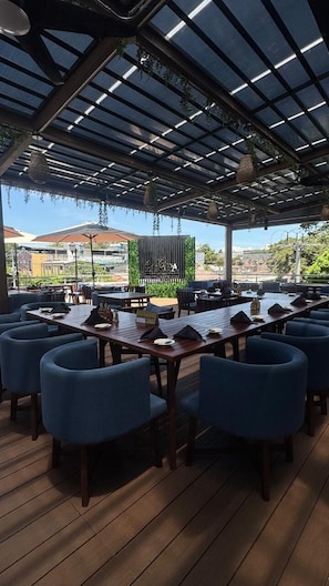 An outdoor seating area with tables and chairs, a covered roof, and a view of the surrounding landscape. - Hotel Arkam (San Salvador)