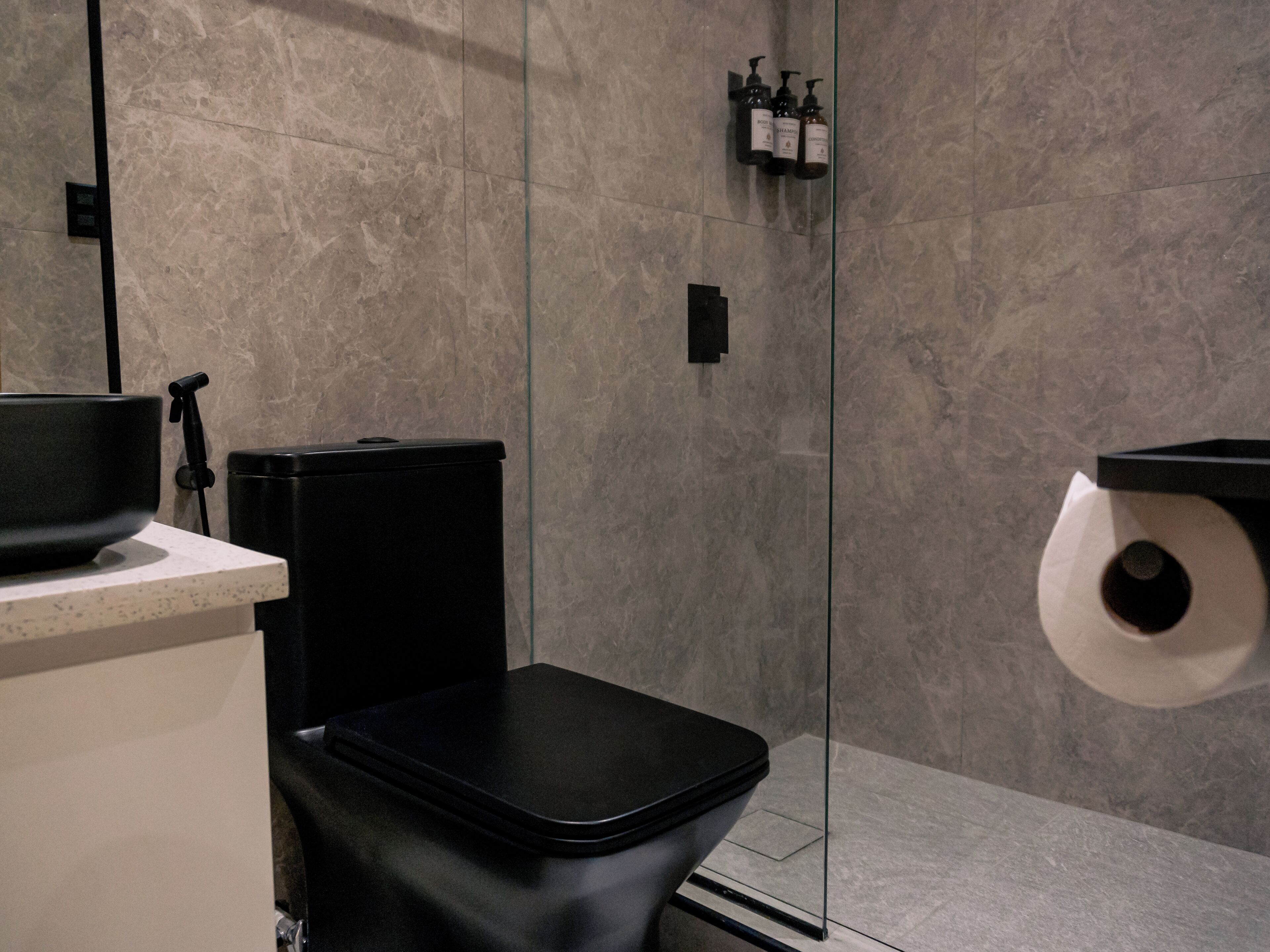 Ein modernes Badezimmer mit einer schwarzen Toilette, einer Duschkabine aus Glas und einem an der Wand befestigten Toilettenpapierhalter.