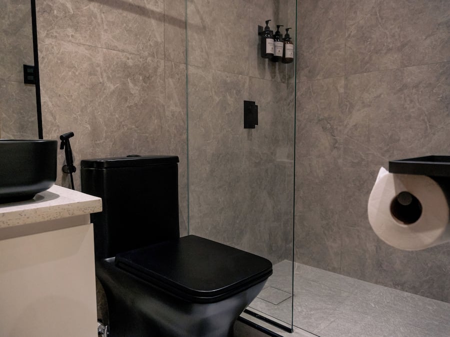 Ein modernes Badezimmer mit einer schwarzen Toilette, einer Duschkabine aus Glas und einem an der Wand befestigten Toilettenpapierhalter.