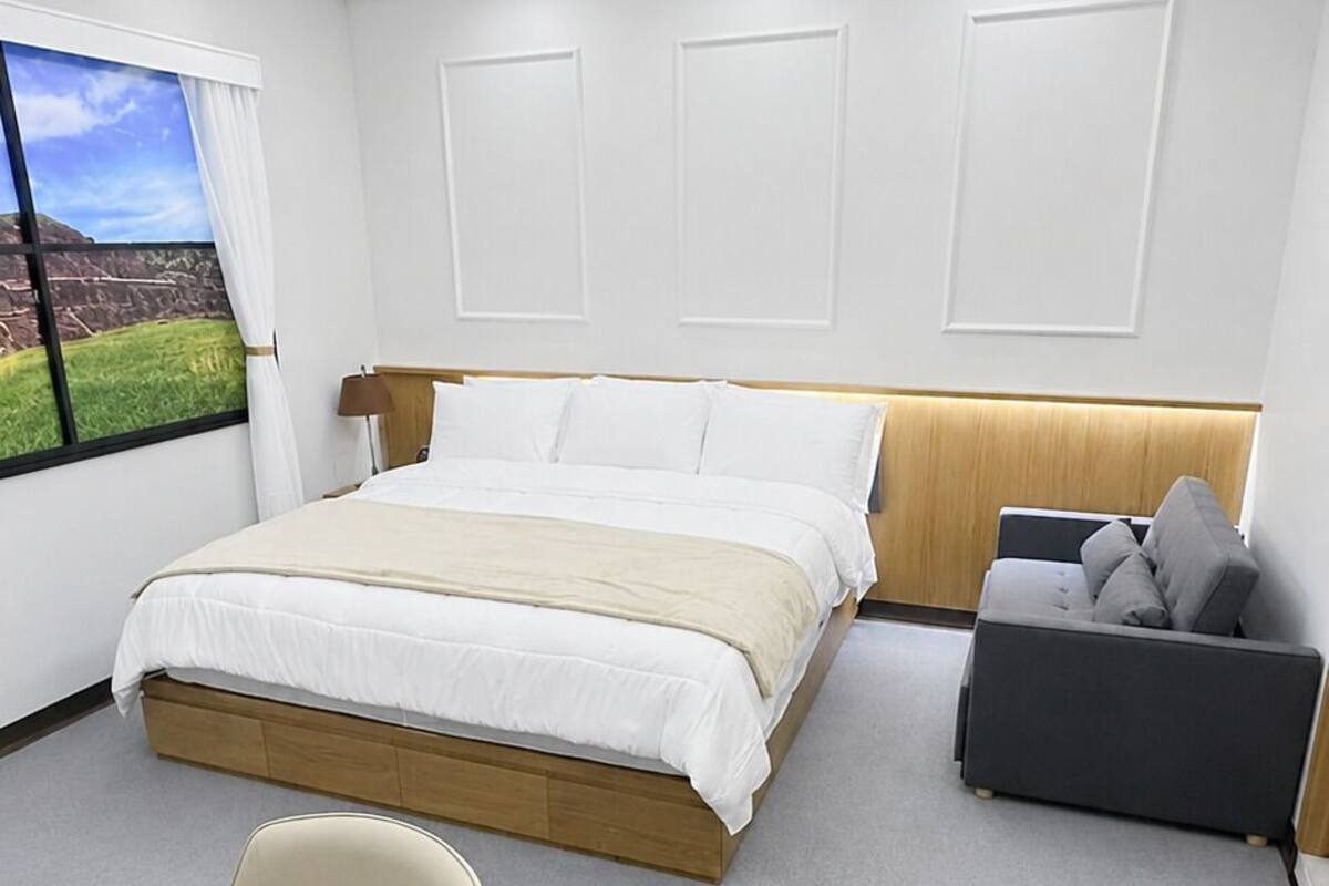 Habitación de hotel moderna con una cama grande, un escritorio, una silla y vistas al exterior.