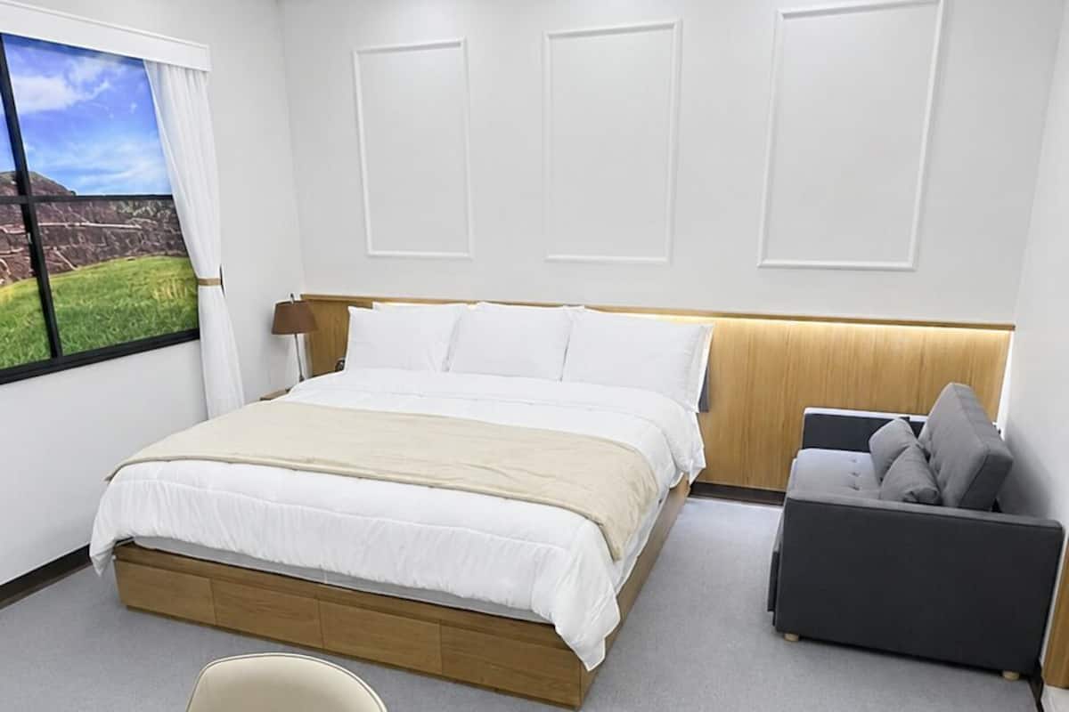 A modern hotel room with a large bed, a desk, a chair, and a view of the outdoors.