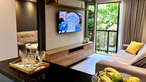 Ett modernt vardagsrum med en tv, en soffa och en matplats med ett brickbord och glas.