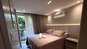 Ett modernt hotellrum med en stor säng, ett nattduksbord, en luftkonditioneringsanläggning och utsikt över grönområden utanför.