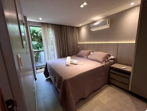 Ein modernes Hotelzimmer mit einem großen Bett, einem Nachttisch, einer Klimaanlage und Blick auf Grünfläche.