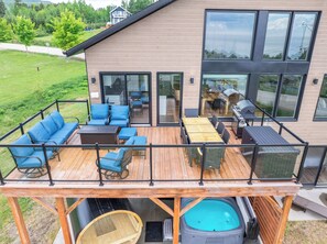 A modern house with a deck, outdoor seating, a hot tub, and a barbecue area. - Spa & Nature | L’Étreinte du Fleuve et des Cimes (Petite-Rivière-Saint-François)