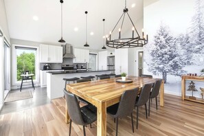 A modern kitchen with a large island, pendant lighting, and a dining area with a wooden table and chairs. - Spa & Nature | L’Étreinte du Fleuve et des Cimes (Petite-Rivière-Saint-François)