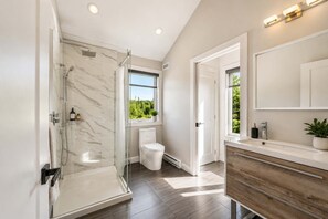 A modern bathroom with a glass shower enclosure, a toilet, a sink with a wooden vanity, and a large mirror. - Spa & Nature | L’Étreinte du Fleuve et des Cimes (Petite-Rivière-Saint-François)