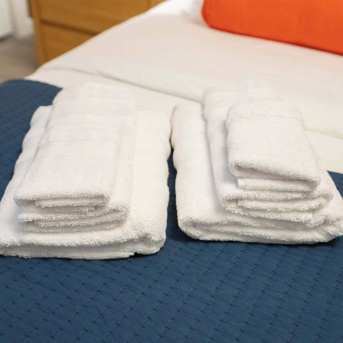 Een bed met een blauwe deken en twee keurig opgevouwen witte handdoeken.