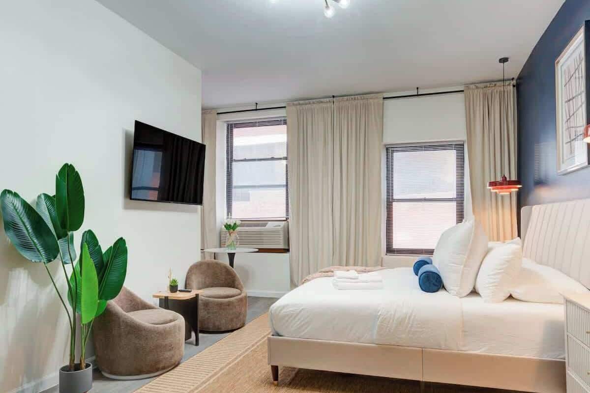A modern bedroom with a bed, a chair, a TV, and a large plant.