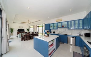 Una cocina moderna con armarios azules, una isla central y un comedor con televisor y plantas.