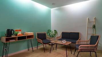 Una habitación con piso de madera, una cafetera negra, sillas de mimbre, una pequeña mesa y una escalera apoyada en la pared.