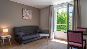 Ein modernes Wohnzimmer mit einem grauen Sofa, einem kleinen runden Tisch, einer Lampe und einem Fenster mit Vorhängen.