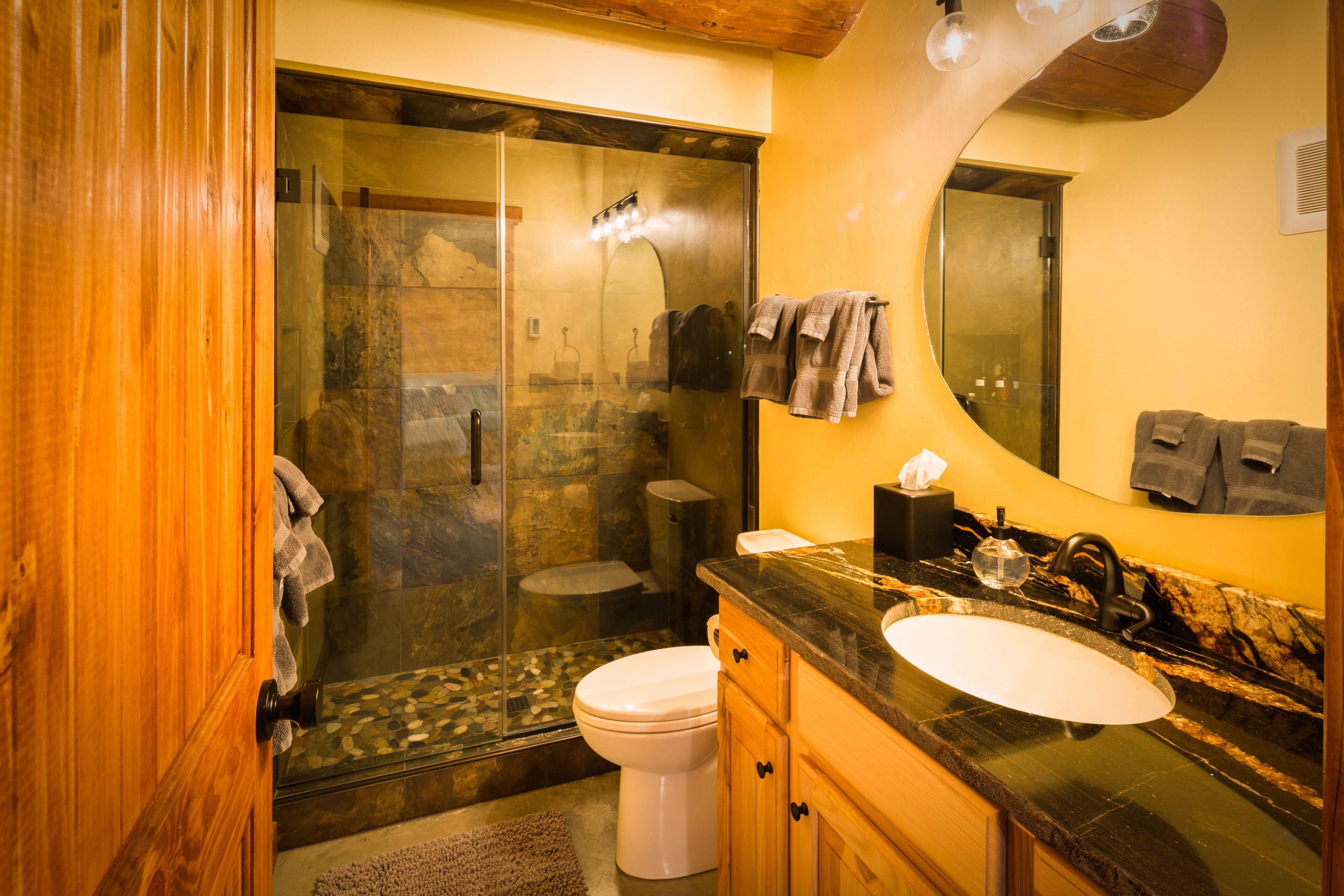 A bathroom with a glass-enclosed shower, a white toilet, a sink with a black countertop, and wooden cabinets.