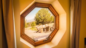 Una habitación con un tragaluz hexagonal que da a un patio con mobiliario exterior y un árbol.
