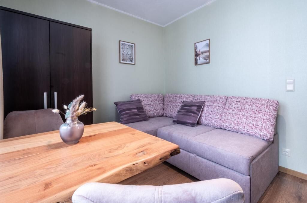 Een kamer met een houten tafel, een grijze bank en een donkere garderobe.