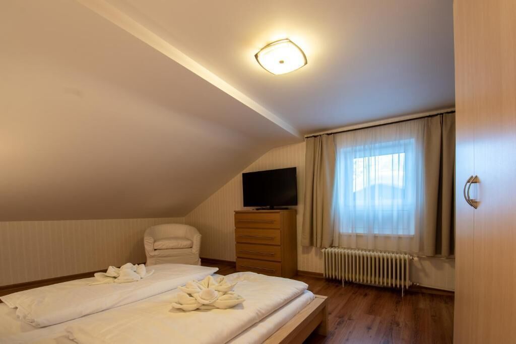 A bedroom with a bed, a chair, a dresser, a television, and a window with curtains.