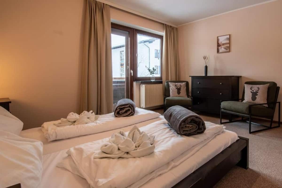 A hotel room with two beds, a dresser, a chair, and a window with curtains.