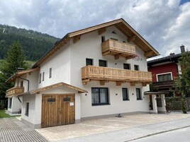 Edificio de dos pisos con balcón de madera, garaje y telón de fondo de montañas.