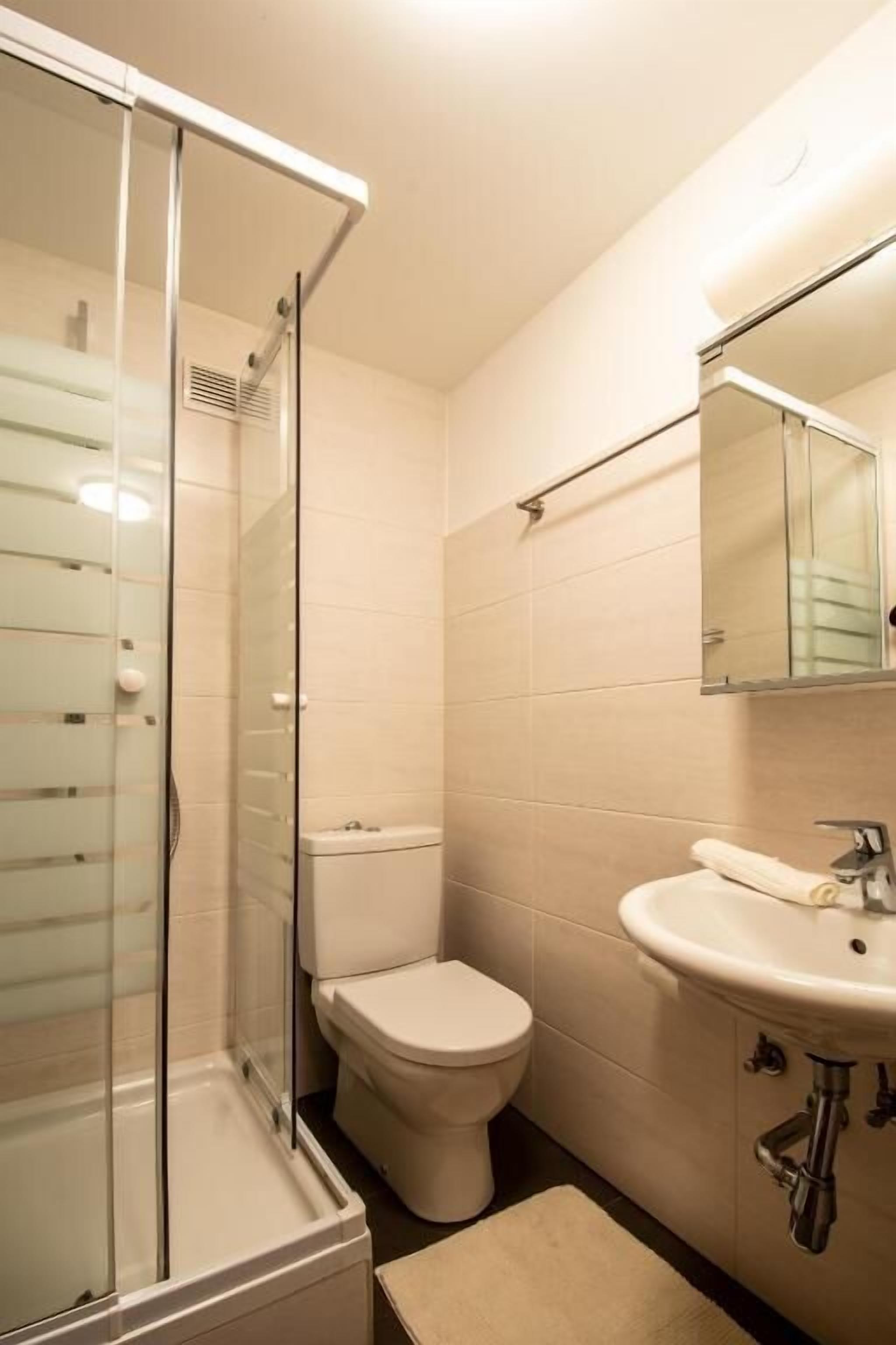 A bathroom with a glass-enclosed shower, a toilet, and a sink with a mirror above it.