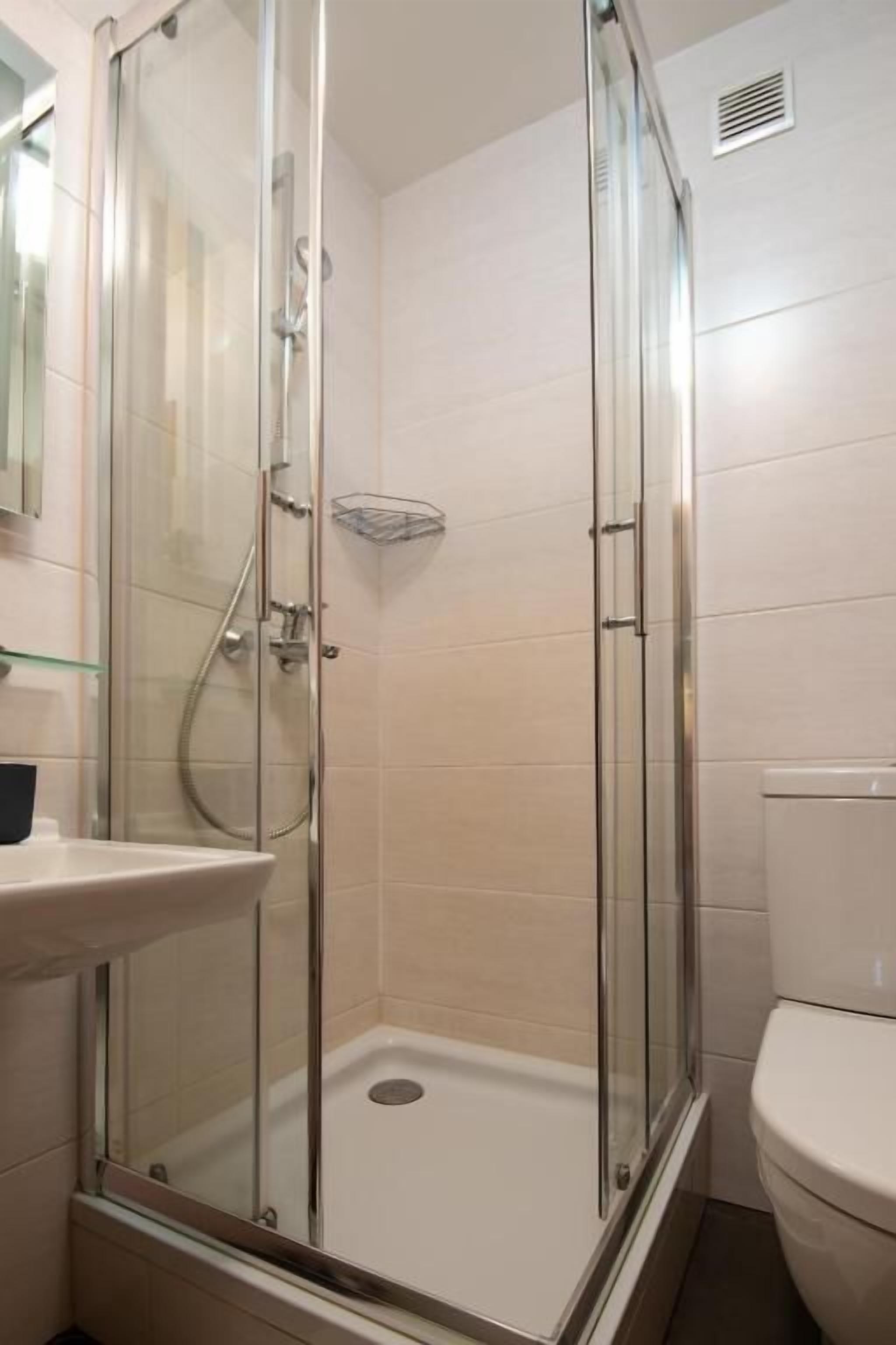 Un baño con ducha de vidrio, inodoro blanco y estante de vidrio.