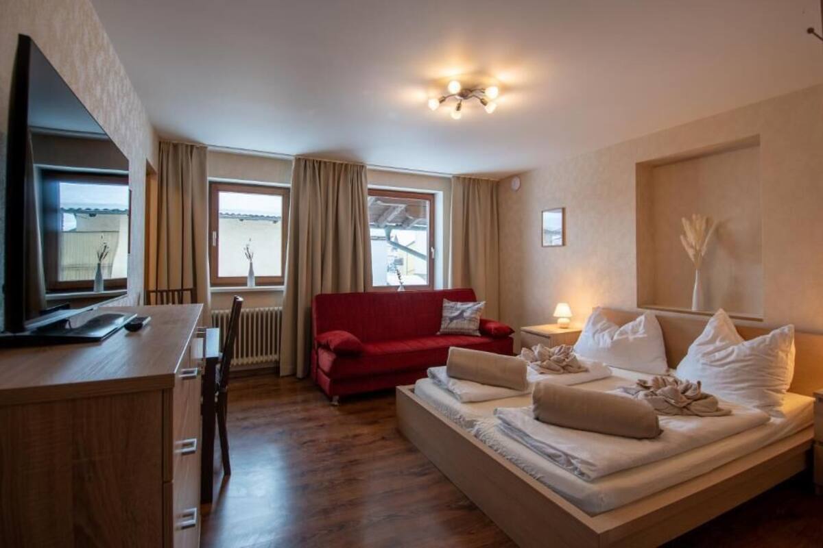 A hotel room with a bed, a red sofa, a TV, and a window with curtains.