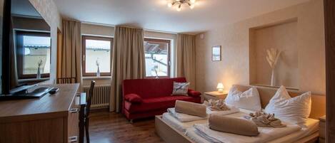 A hotel room with a bed, a red sofa, a TV, and a window with curtains.