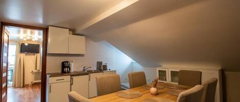 A compact kitchen with a dining area, including a table with chairs, a coffee maker, and a radiator.