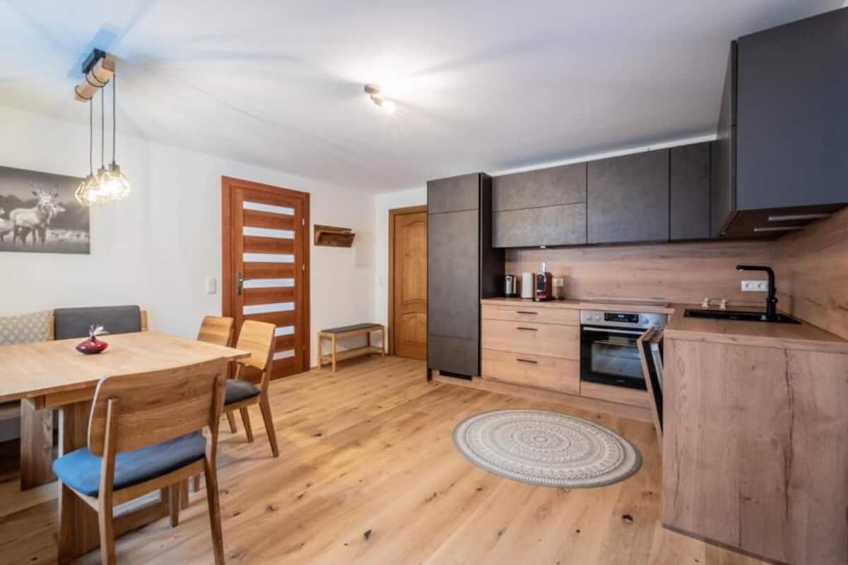 A modern kitchen with wooden cabinets, a built-in oven, and a dining area with a wooden table and chairs.