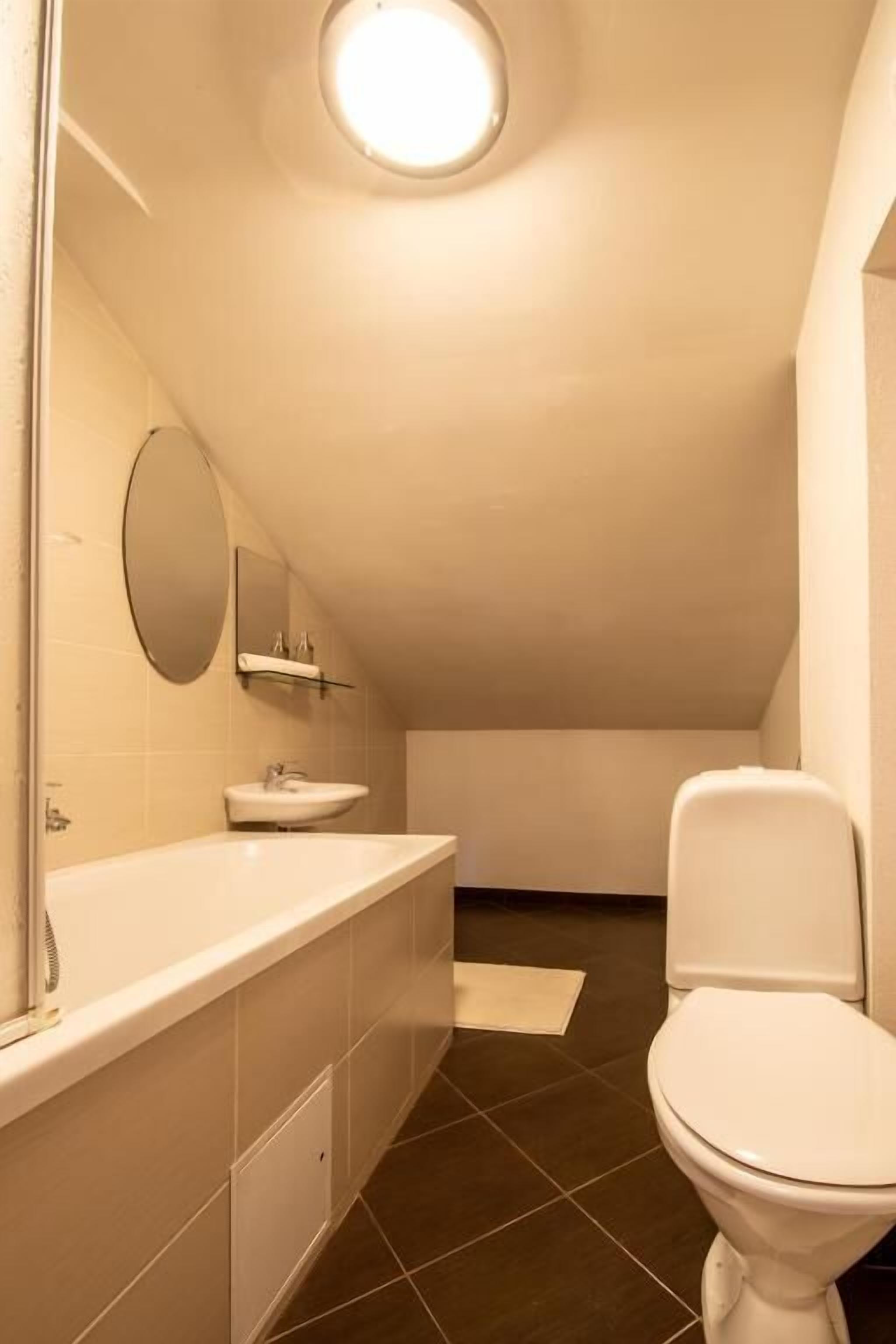 A small, modern bathroom with a white sink, mirror, and toilet.