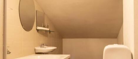 A small, modern bathroom with a white sink, mirror, and toilet.
