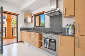 Eine moderne Küche mit Holzschränken, einer eingebauten Mikrowelle, einem Edelstahlherd und einem Fenster mit Blick auf Grünflächen.