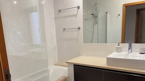Un bagno con box doccia in vetro, una vasca, un lavandino con due flaconi e un portascopevoli.