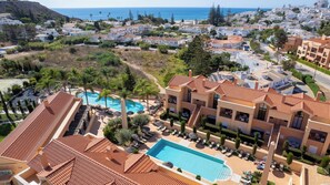 A resort with a swimming pool, sun loungers, and a view of the sea.