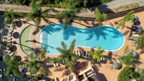 Vista aérea de un resort con piscina rodeada de palmeras y tumbonas.