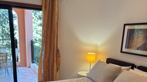 Una camera da letto con un letto, un comodino, una lampada, un quadro incorniciato e vista su un balcone esterno.
