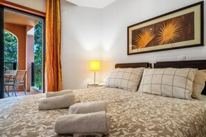 A hotel room with a bed, a nightstand, a lamp, a window with curtains, and a painting on the wall. - Sky Light Bay (Luz)