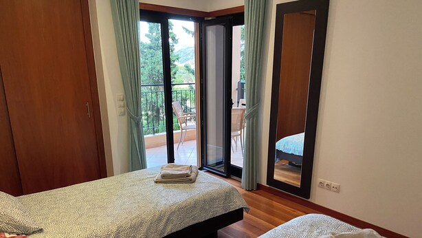 Camera da letto con due letti, una porta finestra con vetri scorrevoli su un balcone e pavimento in legno.