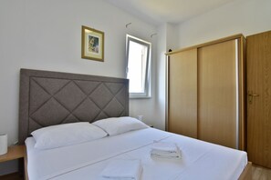 A neatly made bed with white linens and pillows, a wooden wardrobe, a framed picture on the wall, and a window providing natural light. - Equipped Flat Just a Short Walk From the Beach (Novigrad)
