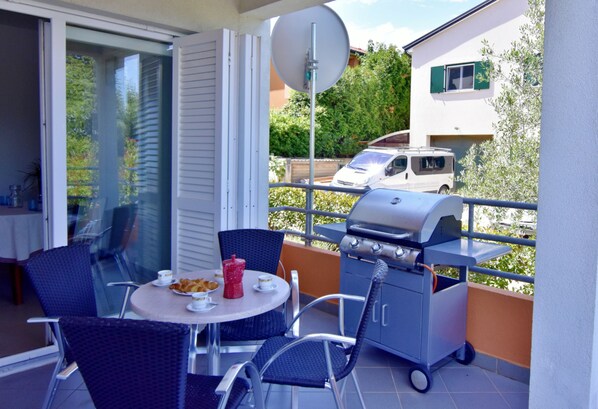 An outdoor balcony with a grill, dining table, chairs, and a view of a parked car and greenery. - Equipped Flat Just a Short Walk From the Beach (Novigrad)