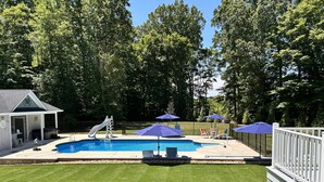 A backyard with a swimming pool, a slide, and a covered seating area with umbrellas. - Olivet Oasis - saltwater pool, hot tub, pond, walking trails, game room (New Kent)