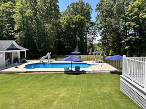 A backyard with a swimming pool, a slide, and a covered seating area with umbrellas.