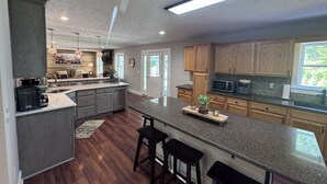 A modern kitchen with granite countertops, wooden cabinets, and a large island with bar stools. - Olivet Oasis - saltwater pool, hot tub, pond, walking trails, game room (New Kent)